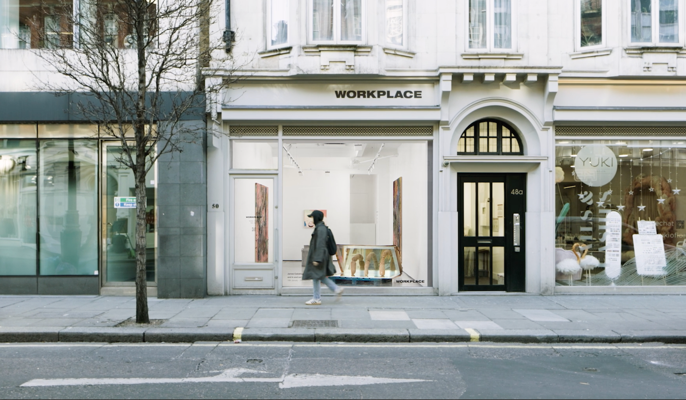 a video still of the exterior of Workplace London, a pedestrian walks past the window